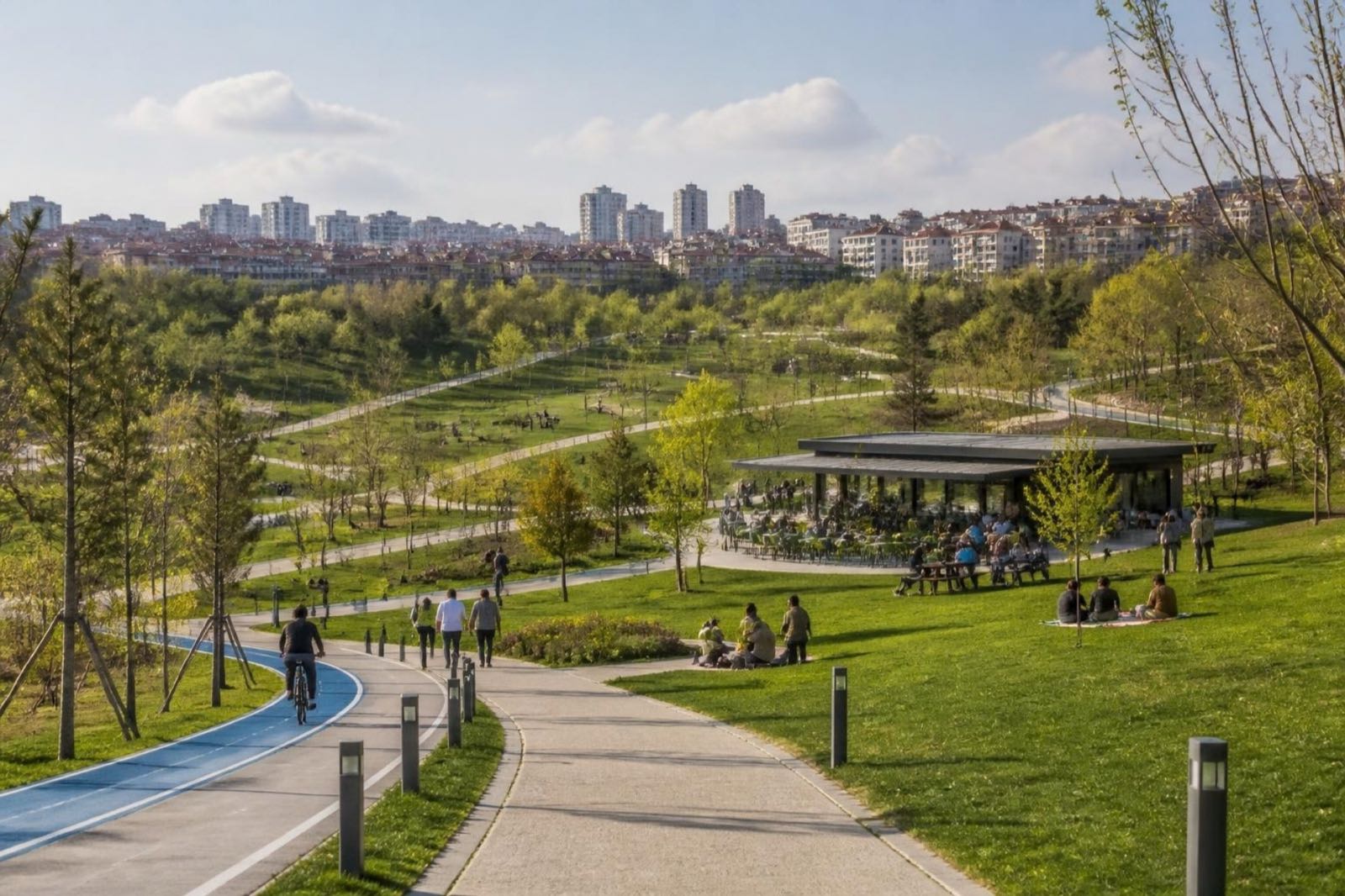 Yürüyüş ve bisiklet yolları, piknik çimenlikleri ve ağaçların ardında apartman blokları bulunan geniş bir yamaç parkı